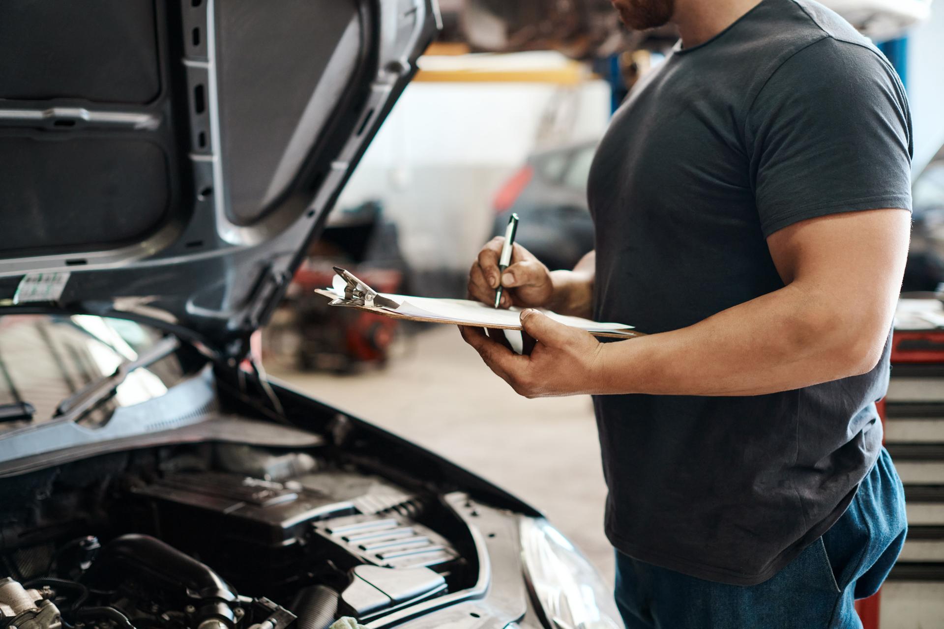 Aufnahme eines Mechanikers, der eine Zwischenablage hält, während er in einer Autowerkstatt arbeitet
