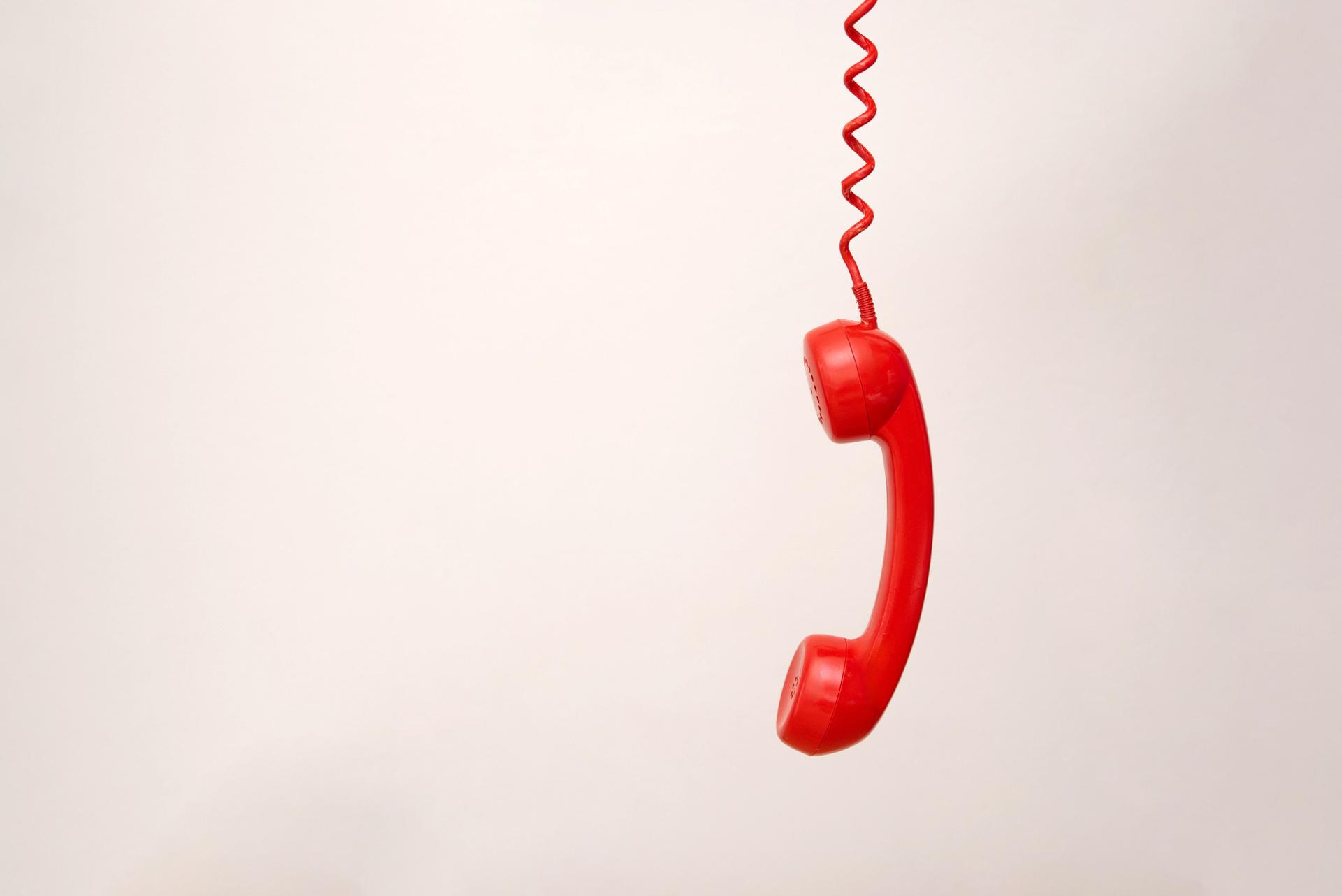 Roter Telefonhörer, der an einer Spiralschnur auf hellgrauem Hintergrund mit Kopierraum hängt