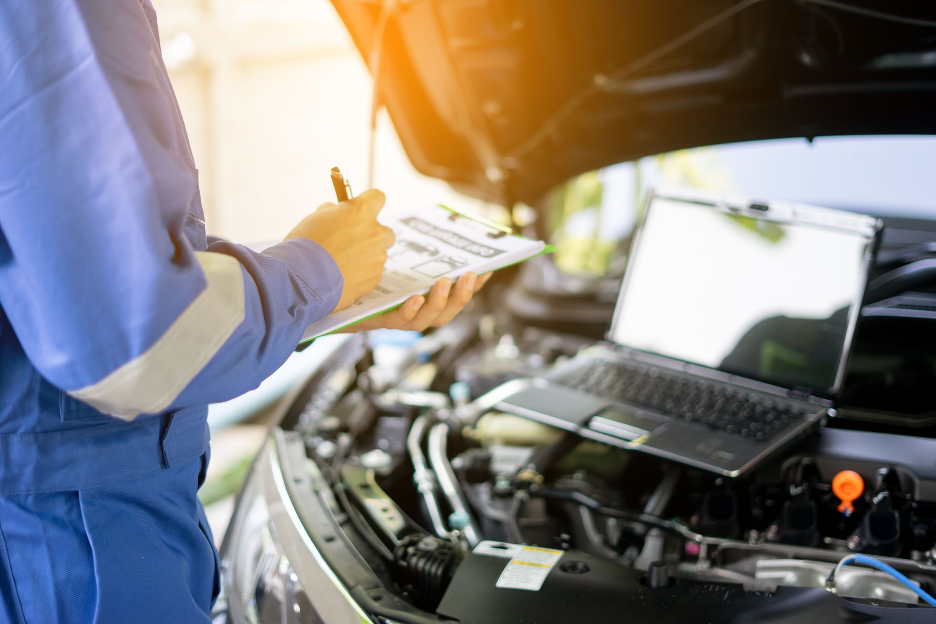 Autoservice, Reparatur, Wartungskonzept - Automechaniker oder Smith schreibt in die Zwischenablage in der Lagerwerkstatt, Techniker macht die Checkliste für Reparaturen Motor ein Auto in der Garage mit Laptop