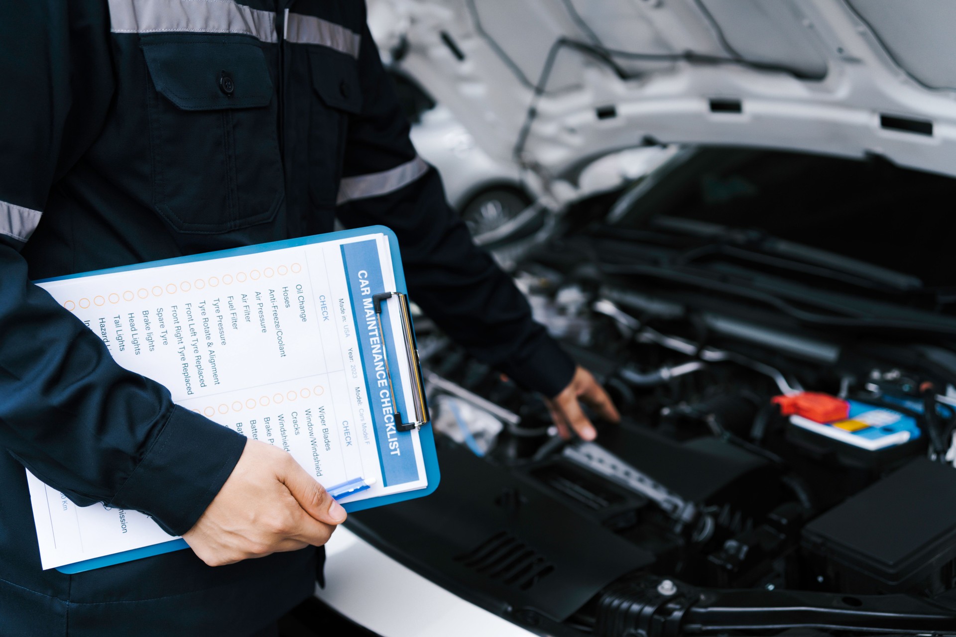 Kfz-Mechaniker, der einen Automotor überprüft, indem er die Checkliste für die Reparatur von Maschinen und Autoservice für Wartung und Wartungsprüfkonzept inspiziert und in die Zwischenablage schreibt.